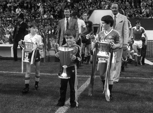 17th August 1983. Martin Buchan Testimonial Match. The Managers Alex Ferguson, Aberdeen, & Ron Atkinson, Manchester United follow the mascots who are holding trophies won in 1982-1983 season